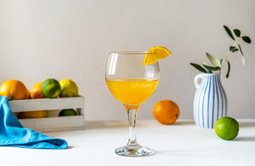 Yellow bird cocktail with rum, orange and lime juice, blue napkin, white box with citrus fruits, vase with olive branch. 