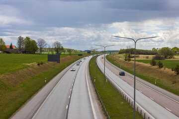 Beautiful top view of highway with several cars. Green side fields and sky with clouds background. Sweden.