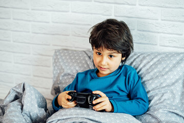 boy playing video games with joystick game console sitting on sofa in living room at home. Gaming video games concept. Little gamer with gamepad