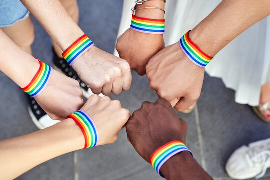 Group of multiracial people putting hands together with LGBT rainbow flag wristbands. Diversity, pride, equality and unity concept.