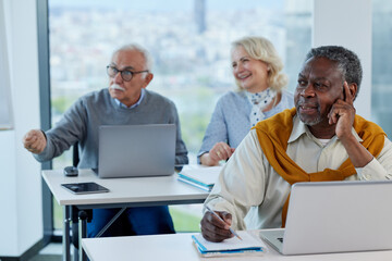 A multicultural senior student is following lecture in a classroom with his classmates.