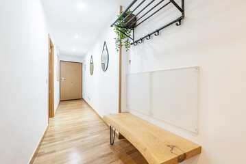 Entrance hall of a residential house with a wooden bench made of a plank with natural varnish and mirrors and a coat rack hanging on the wall
