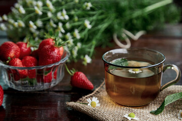 Natural summer breakfast. Organic chamomile tea, antioxidant. Fresh strawberries, chamomile flowers and mint on wooden table. Aesthetic summer lifestyle. Beautiful food. Connecting with nature