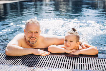 A middle-aged dad and his little son have fun in the pool.