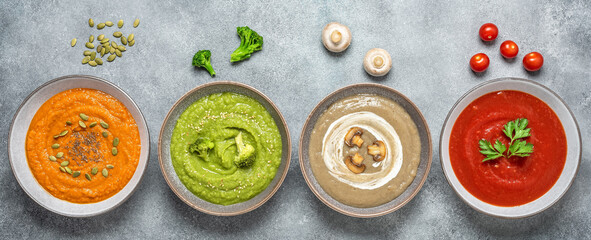 Colored vegetable cream soups. Assortment of vegetarian soups in a line on a gray grunge background. The concept of organic food. Top view, banner.