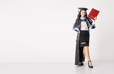 Woman student with diploma on white background with copy space. University graduate indian race woman wearing academic regalia and holding red diploma.