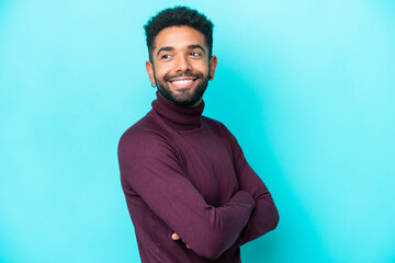 Young Brazilian man isolated on blue background with arms crossed and happy