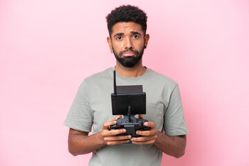 Brazilian man holding a drone remote control isolated on pink background with sad expression