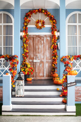 Fototapeta na wymiar House entrance staircase decorated for autumn holidays, fall flowers and pumpkins. Cozy wooden porch of the house with pumpkins in fall time. Halloween design home with yellow fall leaves and lanterns