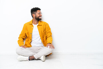 Young Brazilian man sitting on the floor isolated on white background laughing in lateral position
