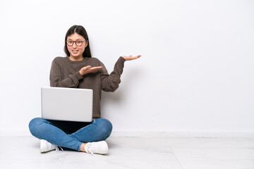 Young woman with a laptop sitting on the floor extending hands to the side for inviting to come - obrazy, fototapety, plakaty