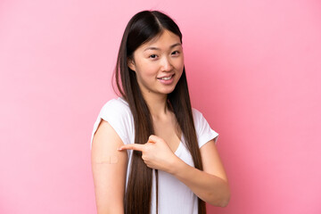 Young Chinese woman wearing a band aids isolated on pink background and pointing it