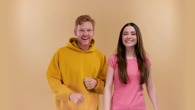 delighted emotional couple celebrate victory raise fists scream yeah wear denim jeans sneakers isolated on a beige background