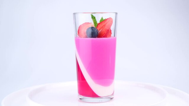 Fruit jelly with strawberries and blueberries in a rotating glass on a white background, a beautiful rotating dessert