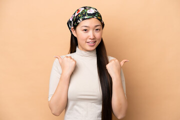 Young Chinese woman isolated on beige background with thumbs up gesture and smiling