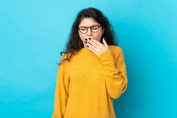 Teenager Russian girl isolated on blue background yawning and covering wide open mouth with hand