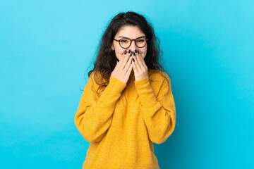 Teenager Russian girl isolated on blue background happy and smiling covering mouth with hands