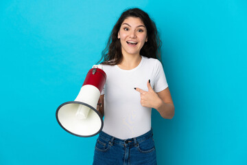 Teenager Russian girl isolated on blue background holding a megaphone and with surprise facial...