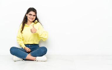 Teenager Russian girl sitting on the floor giving a thumbs up gesture