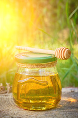 Jar honey and spoon for honey in forest on stump.