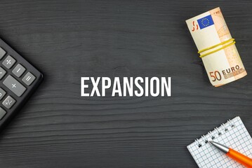 EXPANSION - word (text) and euro money on a wooden background, calculator, pen and notepad. Business concept (copy space).