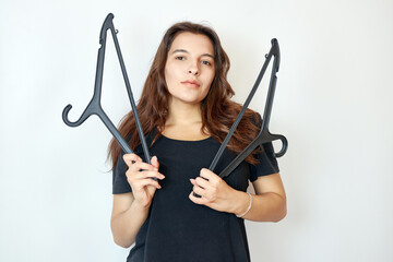 Beautiful girl in a black T-shirt holding two hangers. The concept of choosing and buying clothes.
