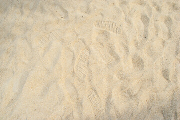 The sand on the beach has shoe marks on the sand.