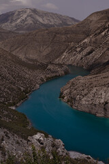 Obraz premium Majestic colorful turquoise blue river and high steep mountain slopes of canyon, clear sky, vertical. Mountain landscape. Hiking, tourism, travel in wild outdoor of Dagestan Caucasian ridges.