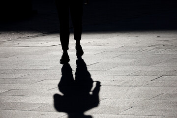 Silhouette of girl walking down the street, black shadow on pavement. Concept of loneliness, city...