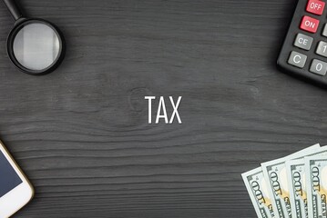 TAX - word (text) and money dollars on the table, phone magnifying glass (loupe) and calculator. Business concept, buying goods and products, paying for services (copy space).
