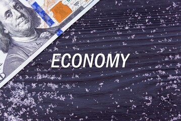 ECONOMY - word (text) on a dark wooden background, money, dollars and snow. Business concept (copy space).