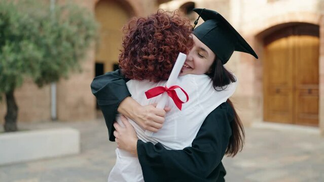 Two women mother and daughter hugging each other holding diploma at campus university