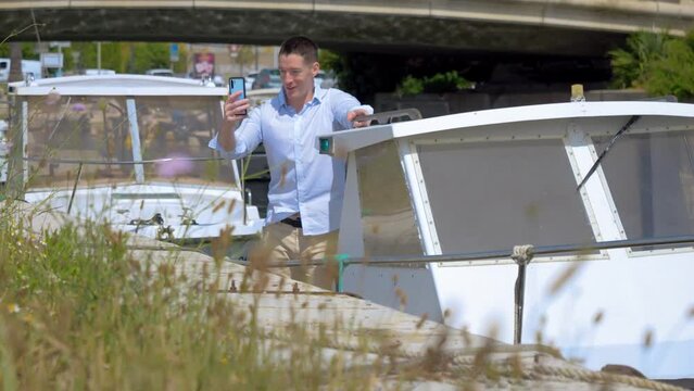 a young Caucasian man on his small boat making a video call with his smartphone