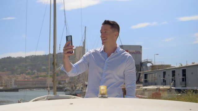 a young Caucasian man on his little boat who picks up his phone to do a live video call