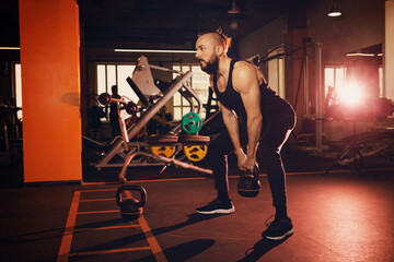 Fototapeta na wymiar Fit young man with a beard in sportswear focused on lifting dumbbells while exercising in the gym.