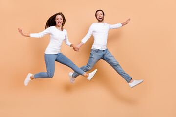 Fototapeta na wymiar Full length body size view of two attractive cheerful partners jumping running isolated over beige pastel color background