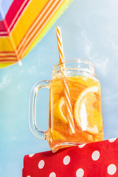 Bottom view of glass mug with frosty orange lemonade, cocktail over blue sunny sky background. Vacation, happiness, summer vibes. Retro style photo
