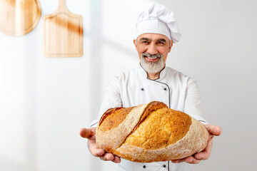 Professional baker offering freshly baked bread. Chef-cooker in a chef's hat and jacket. Senior baker man wearing a chef's outfit. Character kitchener, pastry chef for advertising