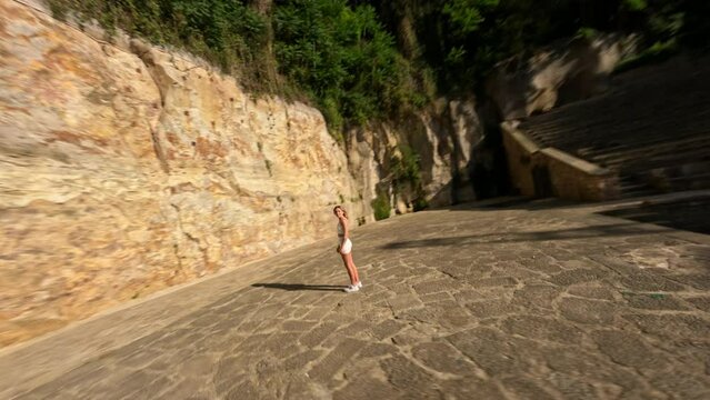 Drone shot of a girl in a white tight suit staying in the ancient amphitheater