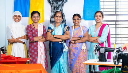 Team of confident woman woman workers at garment standing by arms crossed behind the sewing maching...