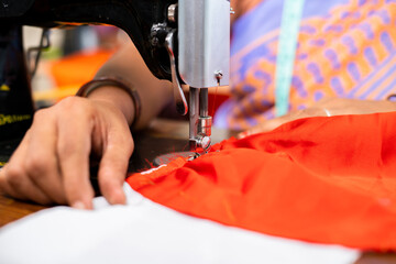 close up, hands of Indian woman at garments busy tailoring or stitching using sewing machine -...