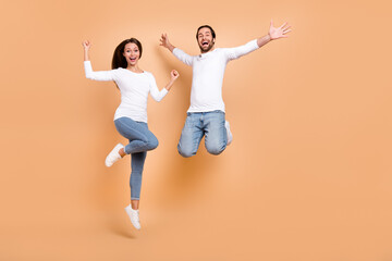 Full length body size view of two attractive cheery spouses jumping having fun isolated over beige...