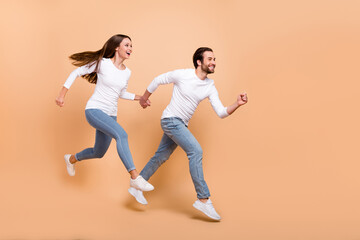 Full length body size view of attractive trendy cheerful partners jumping motion run isolated over beige pastel color background