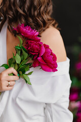 shoulder of a brunette woman in white clothes with a bouquet of peonies.