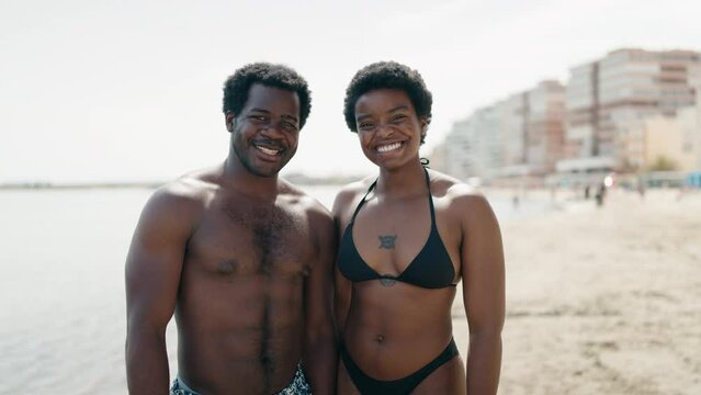 African american man and woman couple wearing swimsuit standing together kissing at seaside