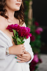 A gentle and peaceful brunette woman in white clothes with a bouquet of peonies.