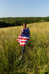 African american woman wrapped in american flag flutters waving in the wind. Happy 4th of July! Independence Day celebrating. Stars and stripes. Freedom concept.

