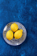 Lemons on blue background. Contrast photo of yellow fruit on textured blue table. Simple...