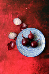 Still life with red onion on vibrant red background with copy space. Onion on a plate. Eating fresh concept. 