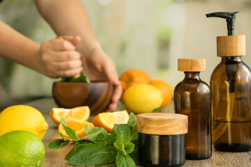 Tree glasses jars with essential oils against background of human hands pounding with pestle in wooden mortar and slices of orange, lemon, leaves of mint. Natural cosmetic concept